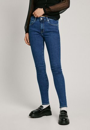 Dunne blauwe spijkerbroek van denim met vijf zakken, een knopenfly en een vervaagde afwerking. Gestyled met een zwarte doorschijnende blouse en loafers.