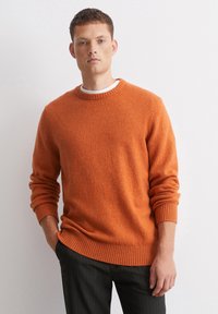 Oranges Strickpullover mit Rundhalskragen und gerippten Bündchen und Saum, kombiniert mit schwarzen Nadelstreifen-Hosen. Texturiertes Gewebe, lässige Passform.