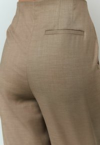 Beige op maat gemaakte broek van een gestructureerde stof. Heeft een slanke, rechte pijp ontwerp en een enkele achterzak.