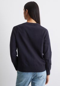 Navyblauwe gebreide trui met een ronde halslijn, geribde manchetten en onderrand. Gladde textuur, lange mouwen en een casual pasvorm. Lichtblauwe spijkerbroek.