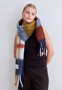 Écharpe multicolore avec des tons jaunes, marine et rouges, en laine douce, avec des franges aux extrémités et une étiquette portant la mention "ARCTIC FOX."