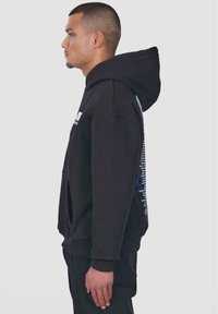 Schwarzer Kapuzenpullover mit seitlichem Logo-Text, entspannte Passform, Kängurutasche und gerippte Bündchen. Glattes Baumwollmischgewebe, minimalistisches Design.