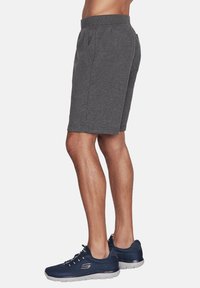 Pantalones cortos deportivos grises hechos de material suave, con una cintura elástica, bolsillos laterales y un corte relajado, combinados con zapatillas navy.