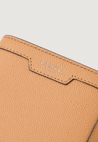 Lancel læderpung i lys orange, med en tekstureret overflade, sort syning og prægede logo i sølvfinish.