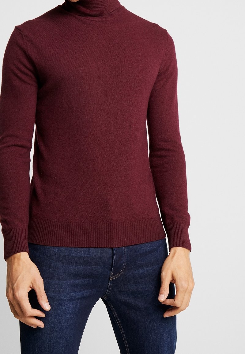 Burgundy turtlenecktröja i stickad syntet, med långa ärmar och ribbade manschetter. Matchad med mörkblå denimjeans.