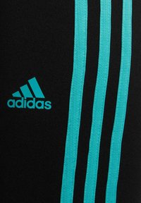 Pantalones deportivos negros con tres rayas verticales azul claro y un logo de adidas en el mismo color. Están hechos de un material elástico y suave.