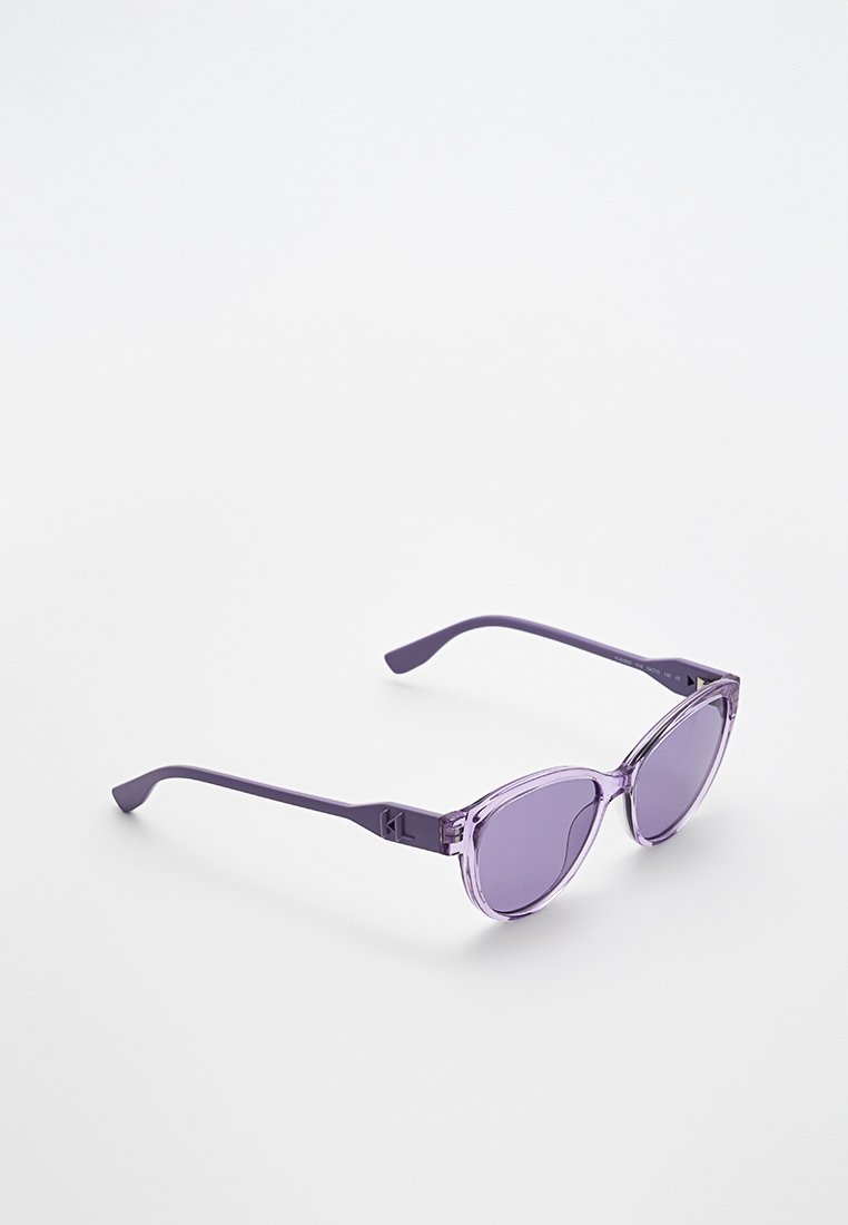 Lunettes de soleil violet en forme d'œil de chat avec des montures transparentes et des verres teintés. Les branches sont fines et comportent un détail de logo près de la charnière.