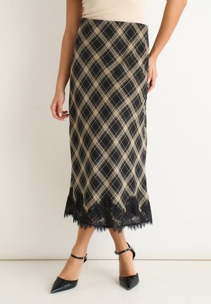 Woman wearing a black and beige plaid midi skirt with black lace hem and black pointed-toe ankle strap heels against a plain background.