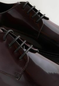 Dunkelburgunderfarbene Lederschuhe mit glänzender Oberfläche, ausgestattet mit schwarzen Schnürsenkeln und kontrastierenden Nähten. Runde Zehenform und glatte Textur.