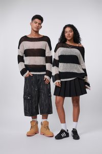 Maglioni a righe in crema, nero e grigio su due modelli. Uno indossa pantaloni cargo neri, l'altro una gonna pieghettata nera. Stivali marroni e sneaker nere.
