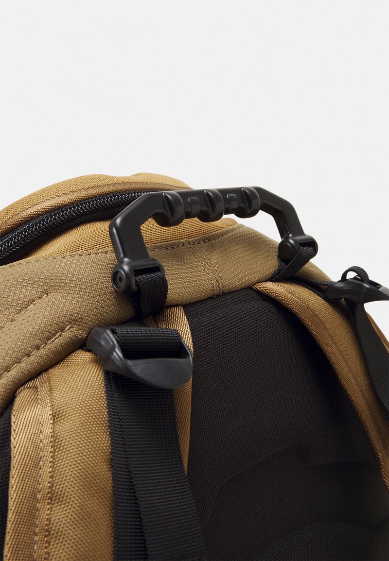 Zaino color sabbia con tessuto testurizzato, hardware nero, una maniglia resistente e spallacci regolabili per diverse opzioni di trasporto.