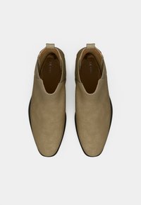 Hnědé semišové kotníkové boty s hladkým povrchem, špičatou špičkou, černou koženou podrážkou a elastickými boky pro snadné nazouvání. Jednoduchý design, bez dalších akcentů.