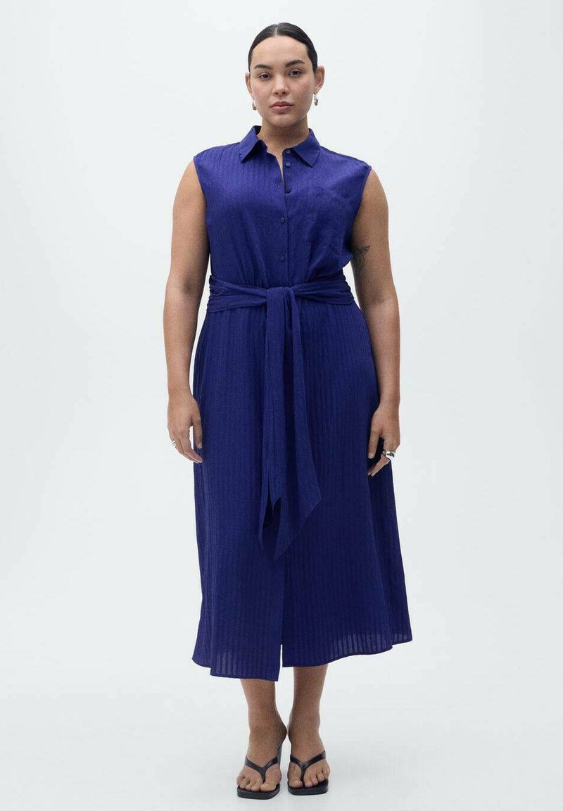 Vestito senza maniche, con bottoni, di un blu intenso e con vita legata. Presenta una texture a costine e una lunghezza midi, abbinato a sandali neri.