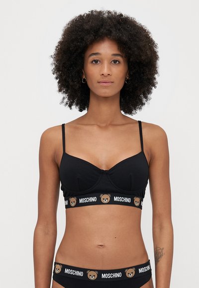 Bralette noir avec fines bretelles, bonnets moulés, arborant un logo ours et une bande "MOSCHINO". Texture lisse, design décontracté.