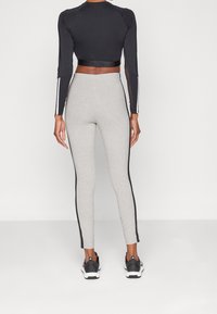 Svart långärmad cropped topp med nätaccenter, tillsammans med ljusgrå leggings med svarta sidostråk. Atletiska skor fulländar outfiten.