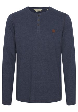 Granatowa koszula henley z długim rękawem, uszyta z miękkiego materiału, z trzema guzikami, kontrastowym przeszyciem i małą brązową naszywką logo na klatce piersiowej.