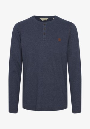 Granatowa koszula henley z długim rękawem, uszyta z miękkiego materiału, z trzema guzikami, kontrastowym przeszyciem i małą brązową naszywką logo na klatce piersiowej.