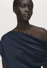 Navy blue draped fabric top with a soft texture, featuring an off-shoulder design and subtle sheen, showcasing the neckline and collarbone.