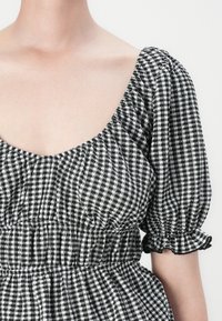 Abito a scacchi bianco e nero con scollatura a barca, maniche a sbuffo e vita arricciata. Tessuto strutturato con bordi delle maniche arricciati.