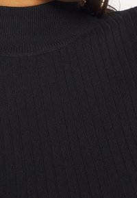 Pull en maille côtelée noir avec col roulé. Présente un col haut et un tissu texturé avec des rayures verticales. Matière douce avec une coupe ajustée.