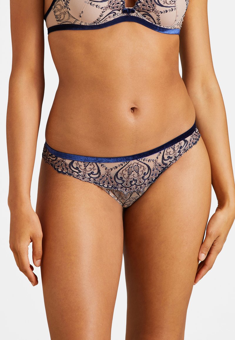 Ensemble de lingerie en dentelle composé d'un matériau transparent beige avec des broderies florales bleu complexes, des accents assortis et un design taille basse.