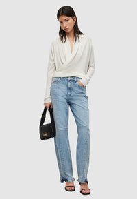 Weißes Crossover-Strickoberteil, hellblaue High-Waist-Jeans, schwarze Handtasche und schwarze Riemchensandalen. Sanfte Texturen und lässige Passform.