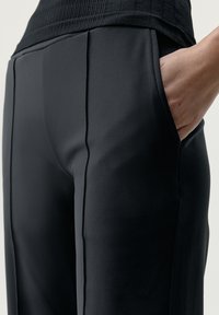 Juodi, lygūs audinio kelnių su pritaikytu siluetu, su šoninėmis kišenėmis ir vertikaliomis siūlėmis, kad suteiktų daugiau struktūros.