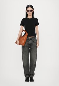 Black fitted t-shirt, high-waisted gray jeans, black chunky boots, and a woven brown bag with a curved handle; sunglasses complete the look.