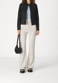 Osoba v černé džískové bundě, světle modrém topu, bílých kalhotách s puntíky, černých platformových sandálech a se černou kabelkou.