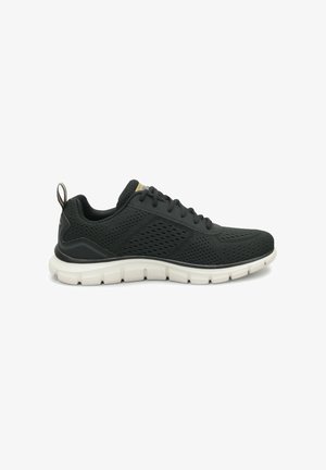 Zapatilla deportiva negra con parte superior de malla transpirable, que cuenta con una suela blanca segmentada y una pequeña pestaña en el talón para facilitar su uso.