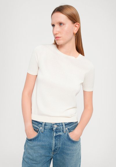 Maglione bianco a maniche corte con scollo rotondo, design aderente e texture morbida, abbinato a jeans in denim blu a vita alta.