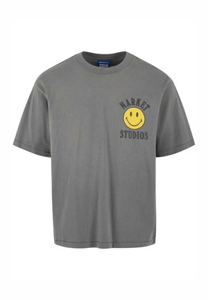 Grå bomulds T-shirt med et gult smilende ansigt grafik til venstre, sammen med teksten "MARKET STUDIOS". Korte ærmer og afslappet pasform.