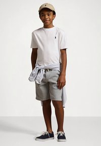 Λευκό polo μπλουζάκι, γκρι σορτσάκι και ναυτικές αθλητικές παπούτσια. Ανοιχτό μπεζ καπέλο και μπλε-άσπρη ρίγα πουκάμισο δεμένο στη μέση. Ανεπιτήδευτο ντύσιμο.