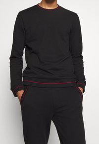 Schwarzer Sweatshirt mit roten Steppnähten am Kragen und an den Bündchen. Verfügt über einen klassischen Rundhals und einen entspannten Schnitt mit geripptem Muster.