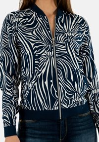 Giacca bomber blu e bianca con motivo a strisce zebra, dotata di zip frontale, polsini a costine e vita aderente.