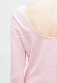 Ροζ μπλουζάκι με μακριά μανίκια που διαθέτει φαρδιά λαιμόκοψη πίσω, ύφασμα από απαλό μείγμα βαμβακιού και λεία υφή. Ο σχεδιασμός τονίζει την απλότητα και το casual στυλ.