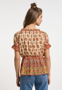 Blusa fluida color crema con motivi floreali in rosso e arancione. Presenta maniche arricciate e una vita arricciata per un tocco di texture in più.