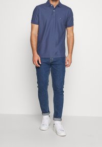 Polo en navy avec un col et une patte de boutonnage à trois boutons, associé à un jean en denim bleu retroussé et des baskets blanches.