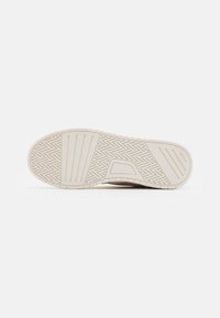 Sole of a sneaker, featuring a textured rubber surface with herringbone and horizontal patterns, primarily in off-white color.