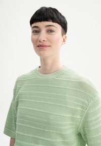 Lichtgroene gebreide trui met een gestructureerd gestreept ontwerp, ronde halslijn en korte mouwen. De stof lijkt ademend en zacht.