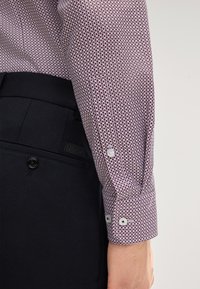 Camicia button-up con un pattern a pois bordeaux e bianchi, in cotone, e con polsini a bottone, abbinata a pantaloni neri su misura.