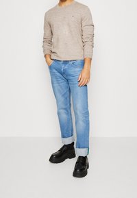 Ljusbeige långärmad tröja, blå raka jeans med uppvikta fållar och svarta chunky-skor med slät textur och minimalistisk design.