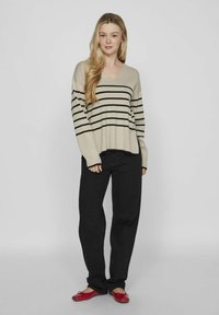 Pullover beige a righe con scollo a V, abbinato a pantaloni neri a gamba larga e ballerine rosse. Tessuto morbido, design casual, vestibilità rilassata.