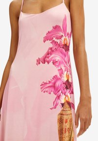 Vestido rosa con tirantes finos que presenta un vibrante estampado floral de orquídeas rosas y un jarrón dorado. Textura de tela suave con un diseño fluido.