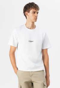 T-shirt en coton blanc à manches courtes, avec un petit imprimé noir sur la poitrine et un col rond. Coupe décontractée.