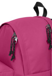 Rosa ryggsäck med strukturerad tyg, med rundad topp, svarta detaljer och dragsko-stängning för säker förvaring.