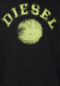 Tessuto nero con il testo usurato in neon giallo "DIESEL" arcuato sopra una forma circolare testurizzata in neon giallo.