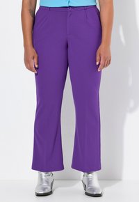 Pantaloni viola a zampa d'elefante con una texture liscia e pieghe frontali, dotati di chiusura con bottone. Abbinati a stivaletti metallici argento a caviglia.