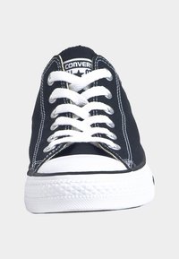 Baskets en toile noire avec semelle en caoutchouc blanche, dotées de lacets blancs, de coutures contrastantes et d'un logo noir et blanc sur la languette.