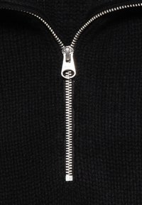 Närbild av en silverdragkedja delvis öppen på svart stickad tyg.